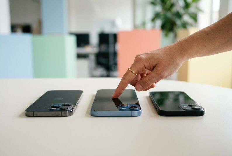 Une main hésite entre trois iPhone reconditionnés posés sur une surface claire pour un choix d'achat.