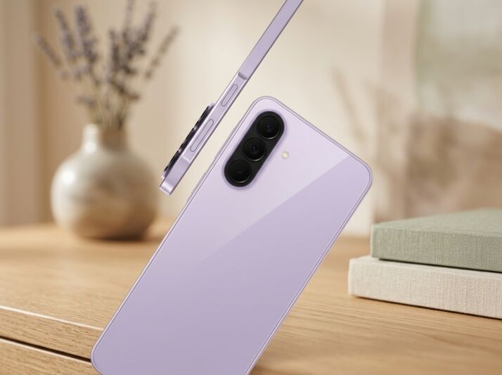 Smartphone violet avec triple capteur photo posé sur une table en bois avec des livres et un vase en arrière-plan.