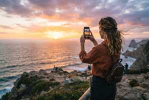 Une femme utilise un smartphone pour photographier un coucher de soleil.