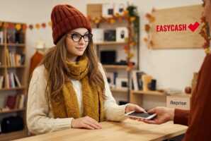 Une cliente en tenue d'automne remet son smartphone à un employé dans un magasin Easy Cash.