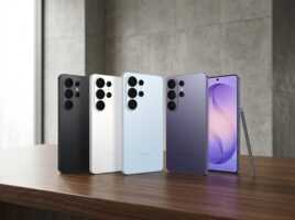 Quatre smartphones Samsung de couleurs différentes alignés sur une table en bois devant un mur en béton.