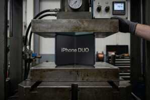 Un smartphone pliant iPhone DUO placé sous une presse hydraulique industrielle pour un test de résistance.